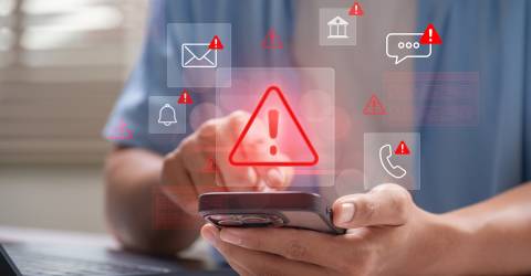 Man achter laptop met telefoon in de hand waarop allerlei phising meldingen gegeven worden